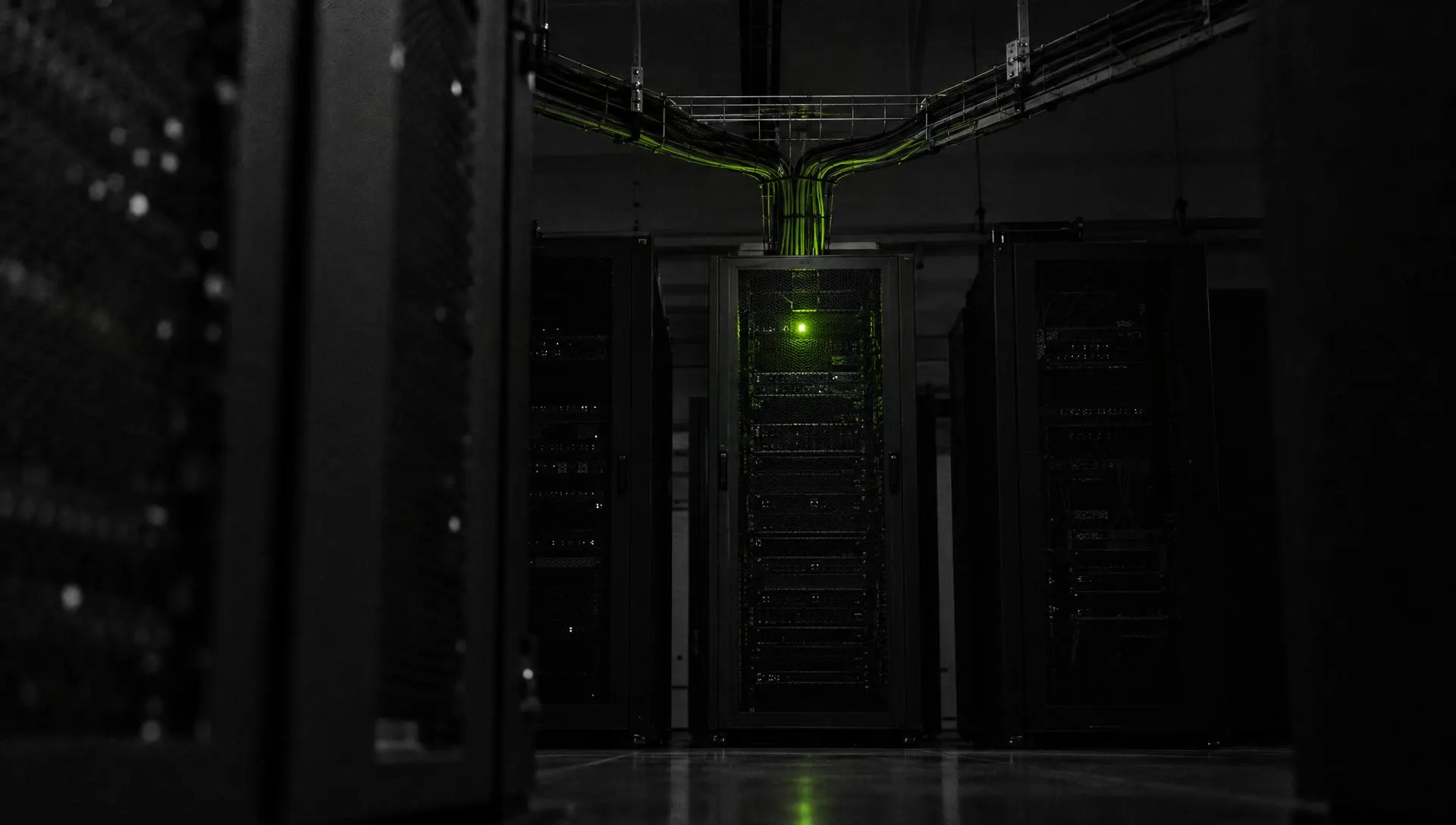 A server-room aisle at night, an overhead cable tray splitting into three bundles above one green status light