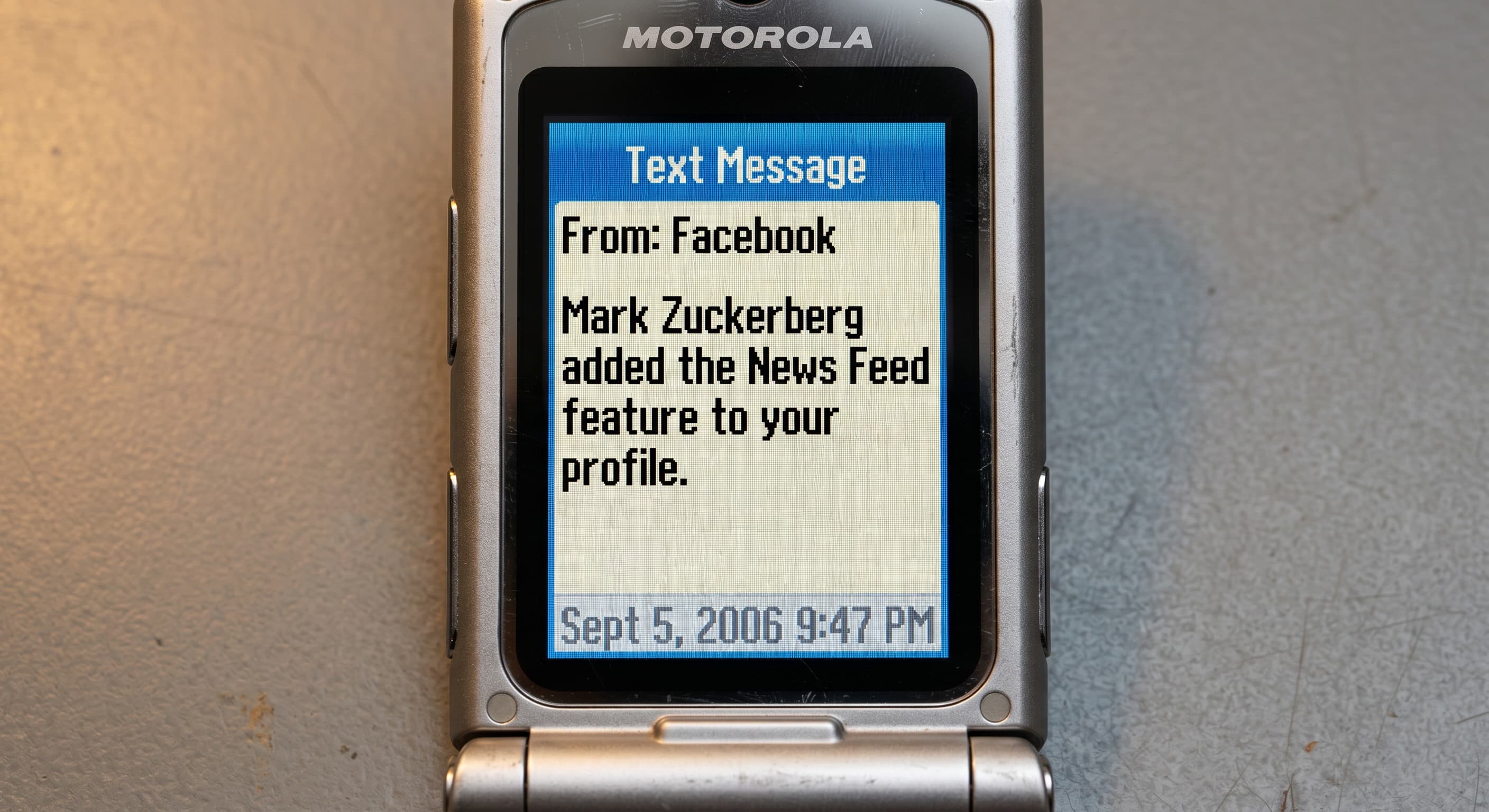 A Motorola RAZR showing a 2006 SMS about Facebook News Feed.